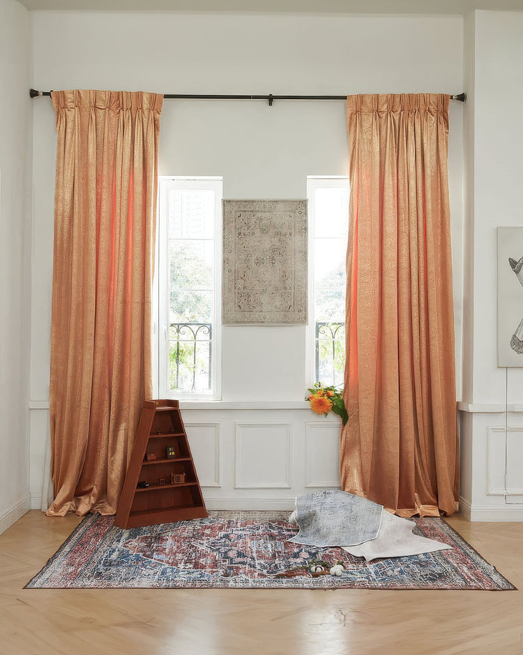 Shimmering orange Palma Foil Printed Velvet custom drapery with elegant pinch pleats, enhancing luxury window treatments in a sunlit room.