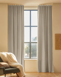 Soft grey Latvian linen blend custom curtains with elegant pleat header framing a tall window, offering light control & sophisticated home aesthetics.