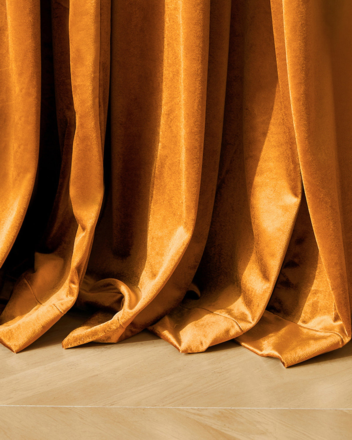 Luxurious golden Moonlit Velvet custom curtain drapes elegantly onto a light wood floor, highlighting the rich fabric & precise tailoring.
