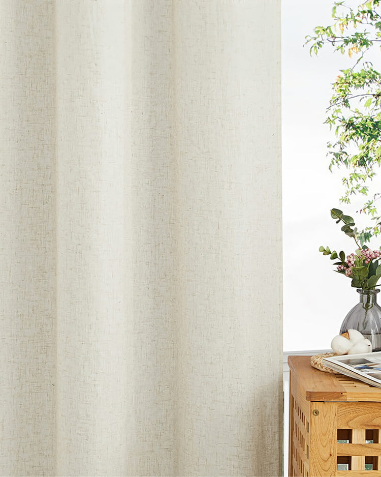 Creamy beige Noah linen-look custom outdoor curtain with visible textured fabric, beside a window with green foliage.