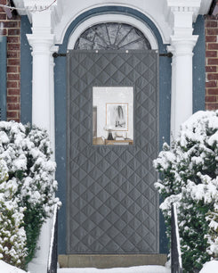Gray quilted custom Oxford thermal door curtain with a PVC window on a snowy front door, providing insulation and soundproofing.