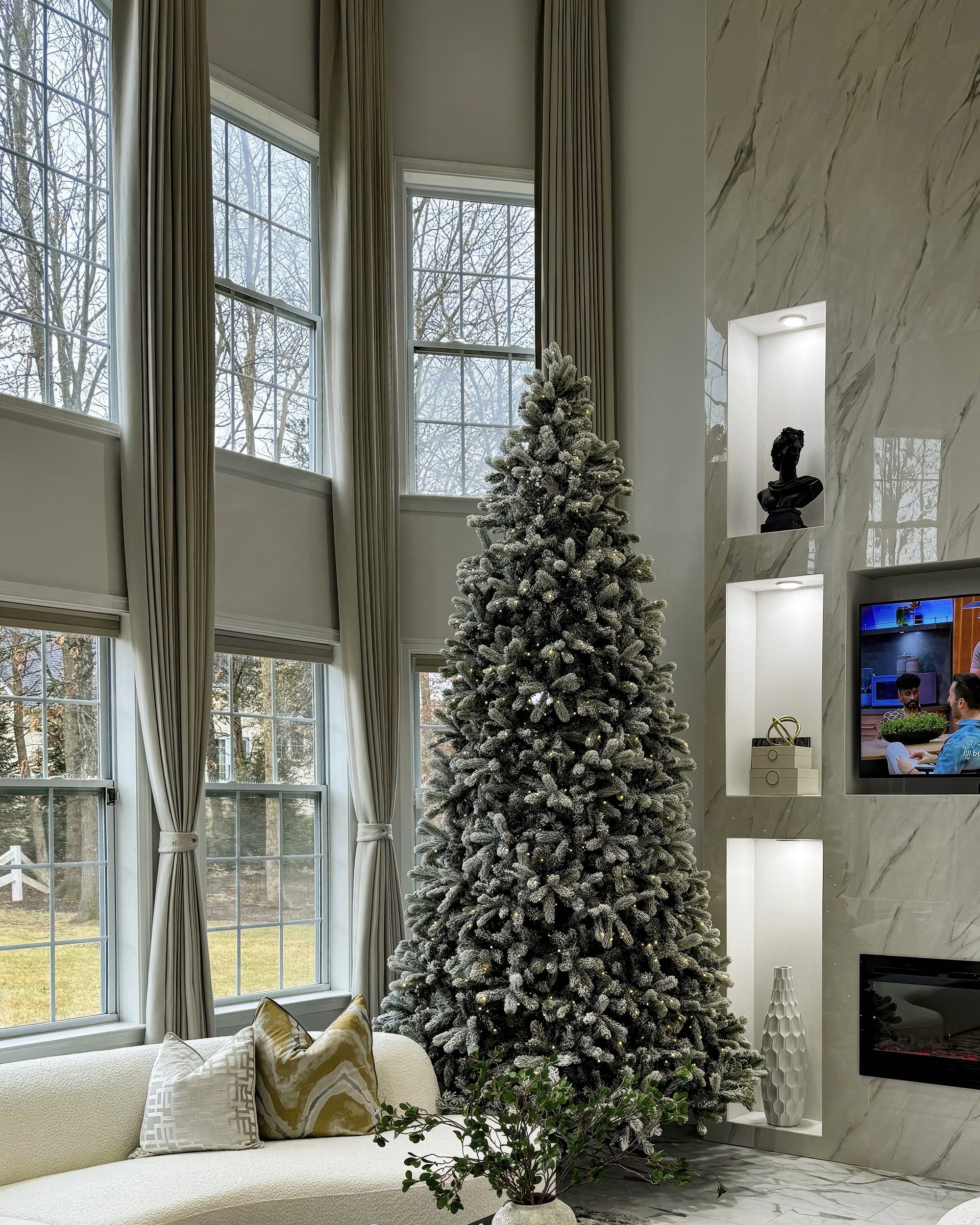 Elegant living room with custom linen-look drapery. Soft beige, floor-to-ceiling curtains tied back, flanking tall windows with a flocked Christmas tree.