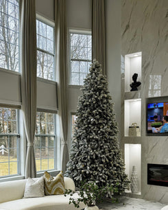 Elegant living room with custom linen-look drapery. Soft beige, floor-to-ceiling curtains tied back, flanking tall windows with a flocked Christmas tree.