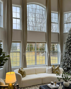 Custom linen-look blackout thermal drapery on tall, arched windows, offering soundproofing & light control for a luxury living room.