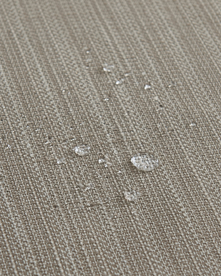 Close-up of waterproof beige custom outdoor curtain fabric, showing water droplets beading on its crisscross woven textured pattern.