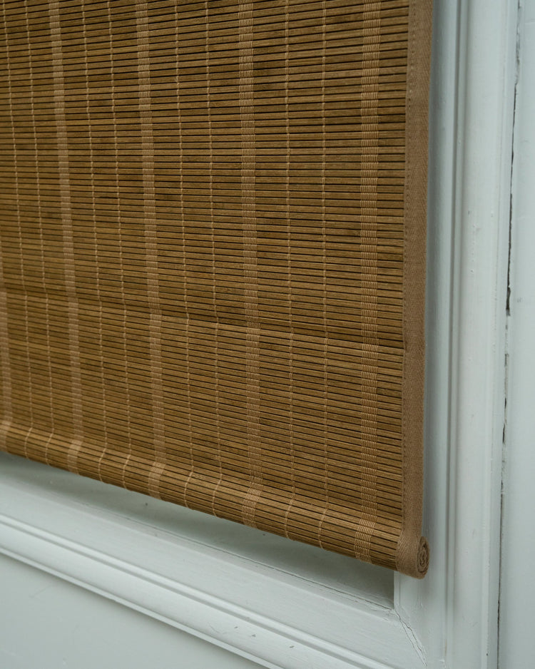 Close-up of Hana tan bamboo woven shade, partially rolled to reveal intricate texture, providing natural light control for windows.
