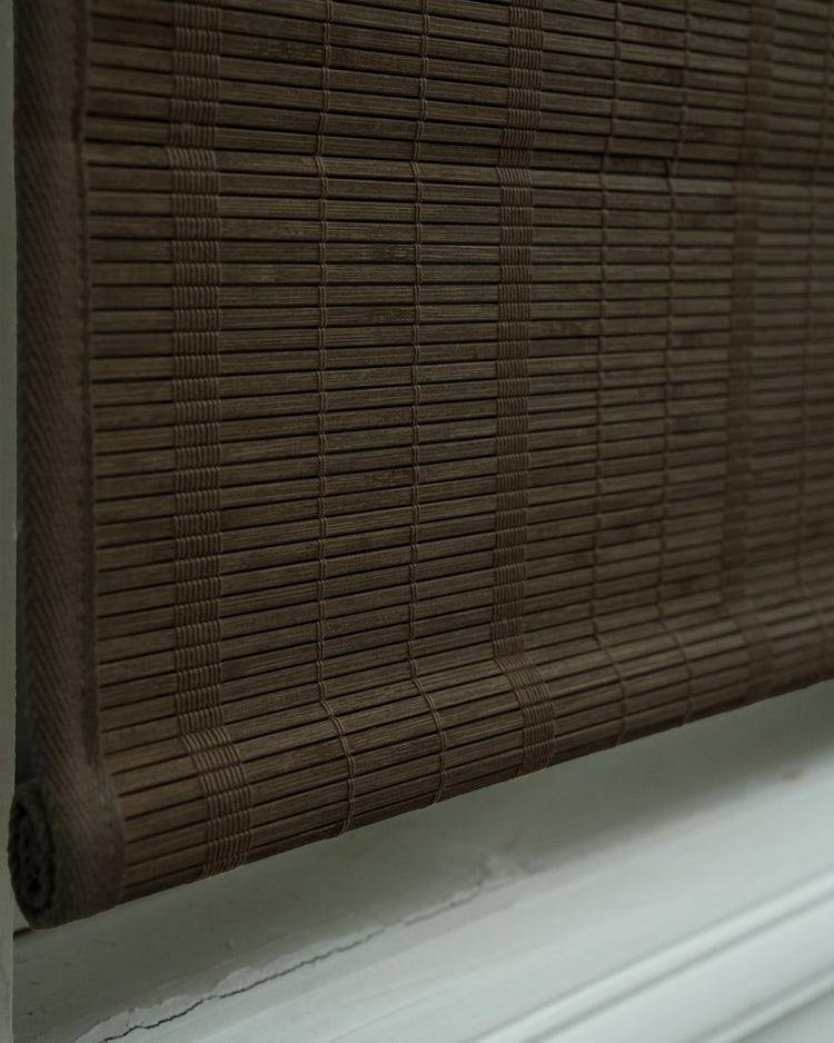 Close-up of a dark brown Hana Bamboo Woven Shade in Bark, highlighting its natural woven bamboo texture and rolled bottom.
