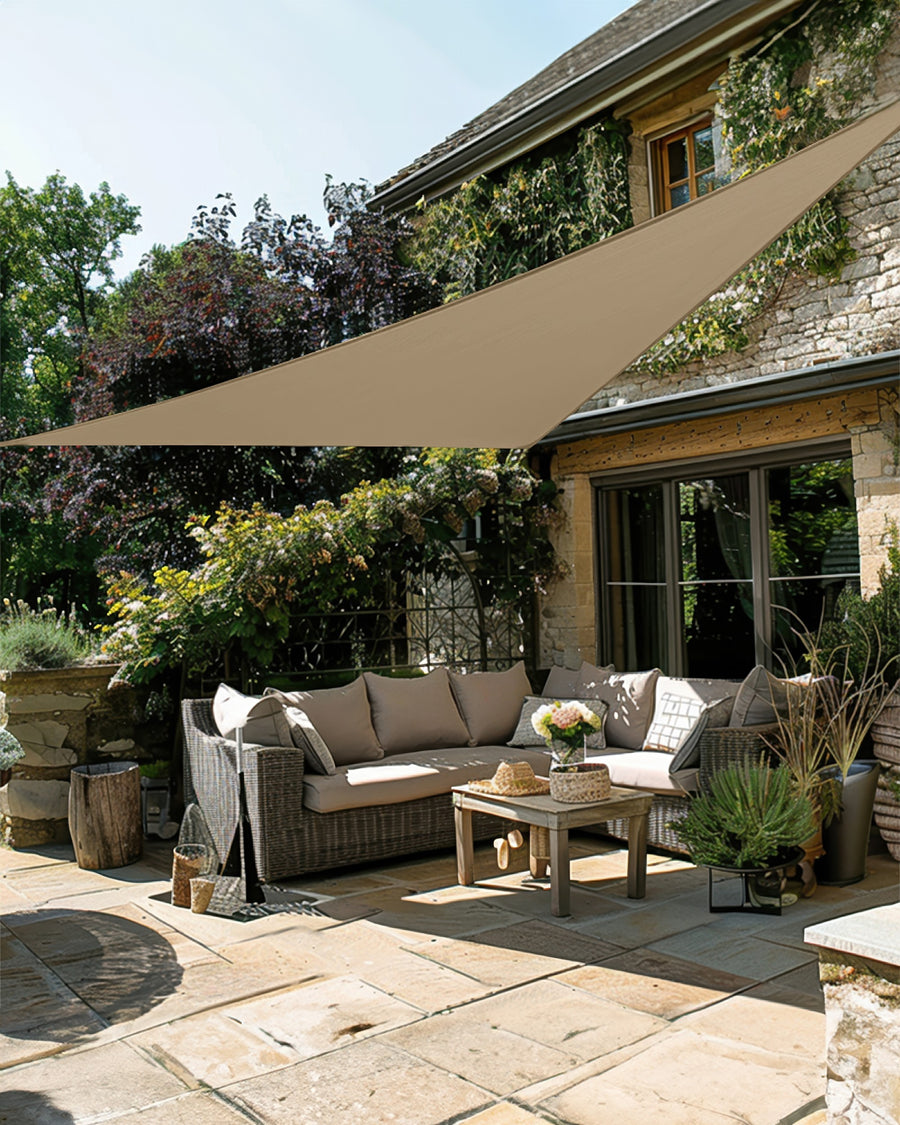 Elegant beige UVShield waterproof custom triangle sun shade sail providing luxury light control over a sunny patio with outdoor sofa.