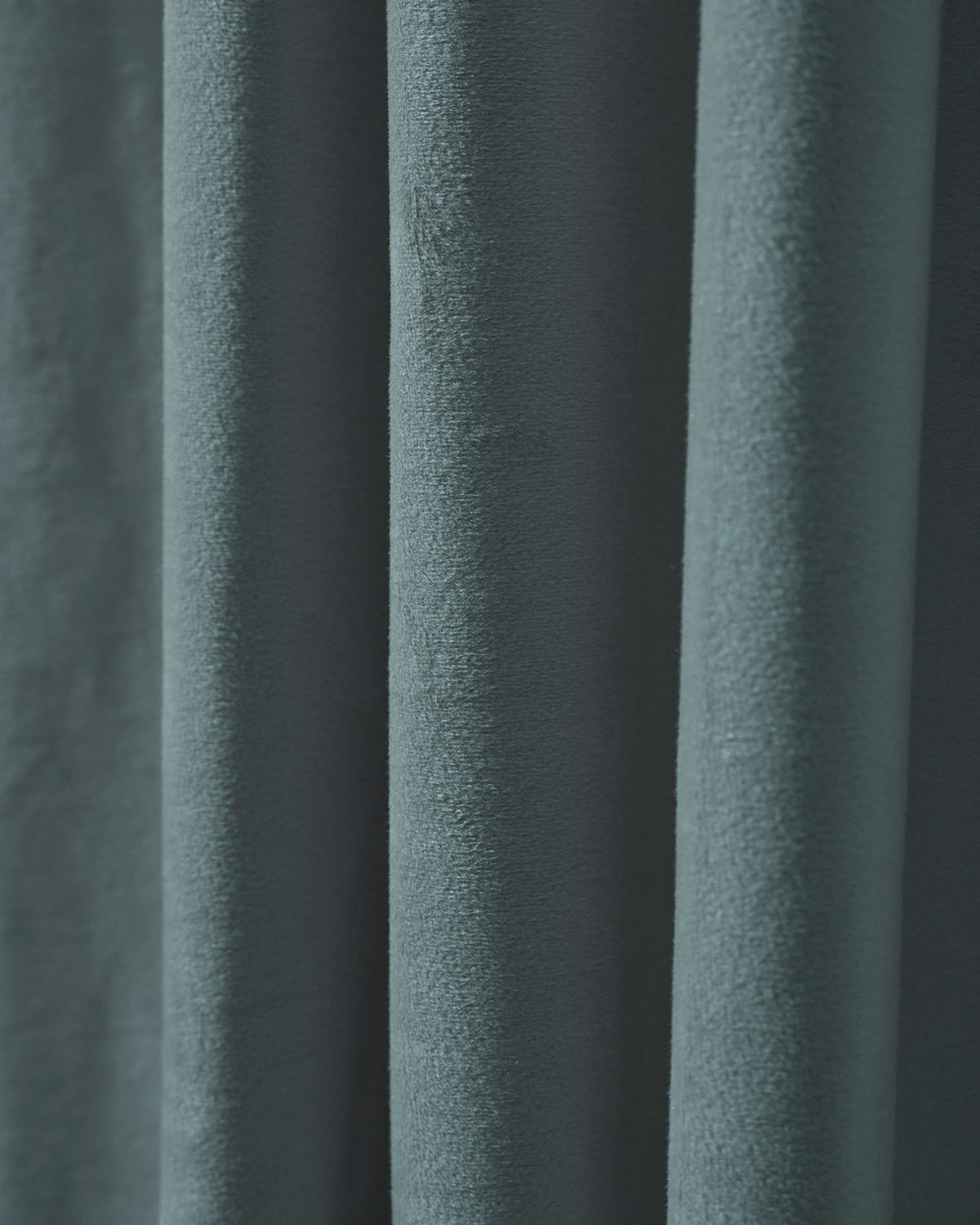 Close-up of a luxurious dusty teal velvet custom blackout curtain, highlighting its plush, heavyweight texture and elegant deep folds.