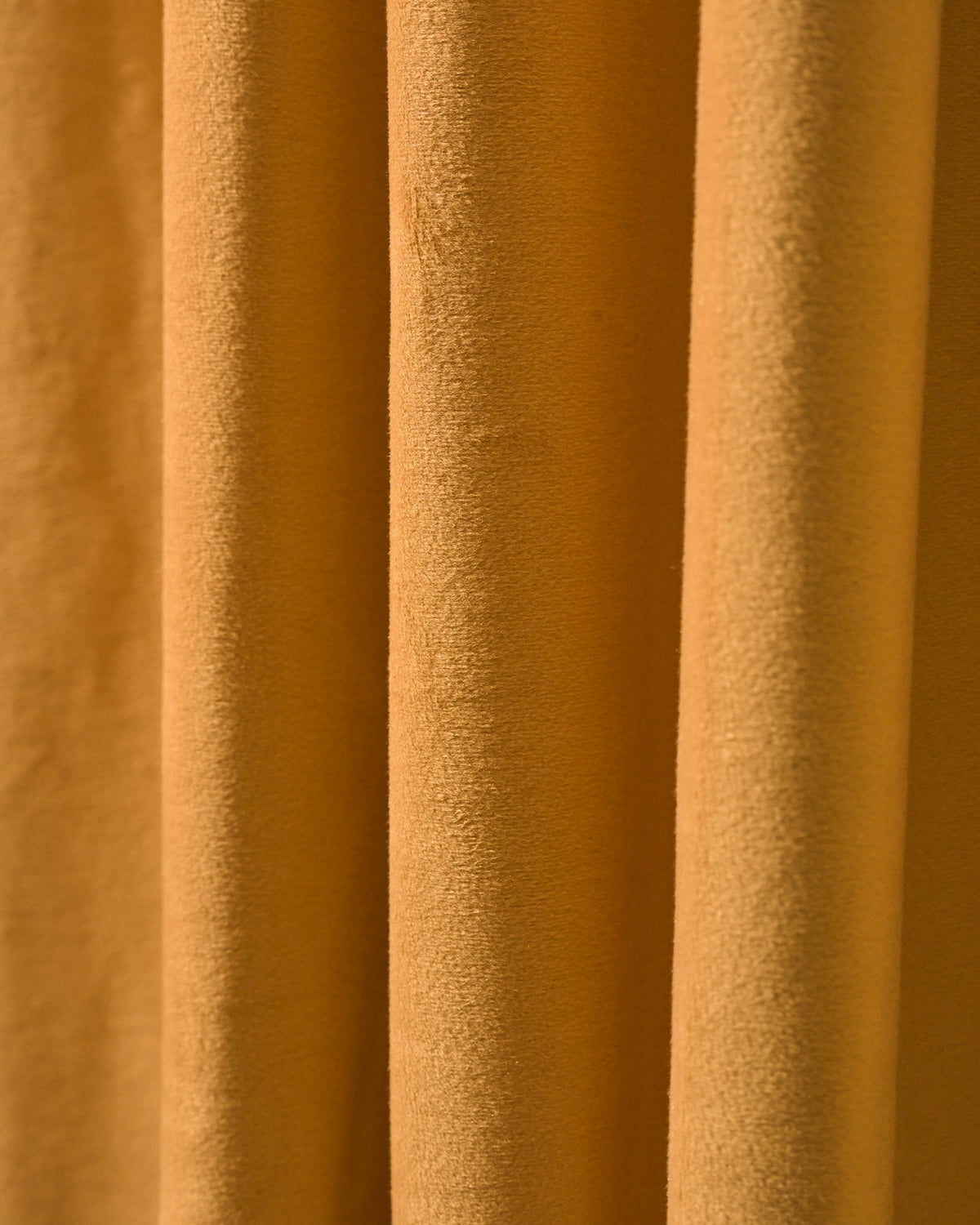 Detailed close-up of golden velvet custom blackout curtain fabric, highlighting its plush, heavyweight texture and elegant folds.