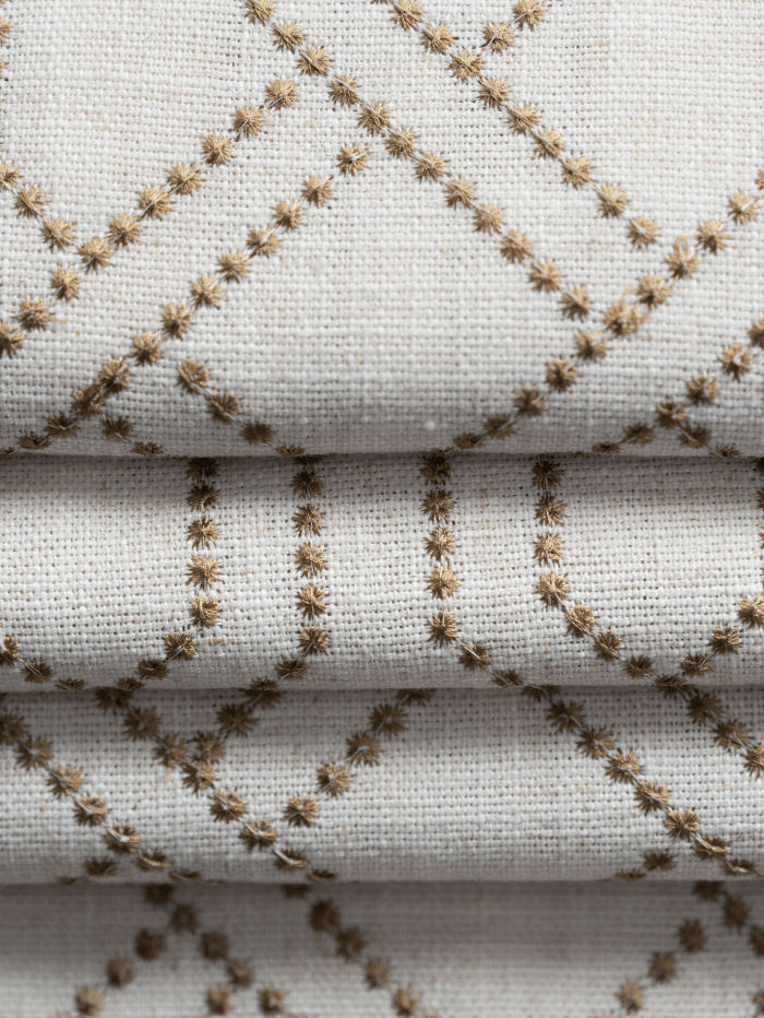 Close-up of cream linen blend fabric with gold interlace geometric embroidery on a flat fold custom Roman shade.
