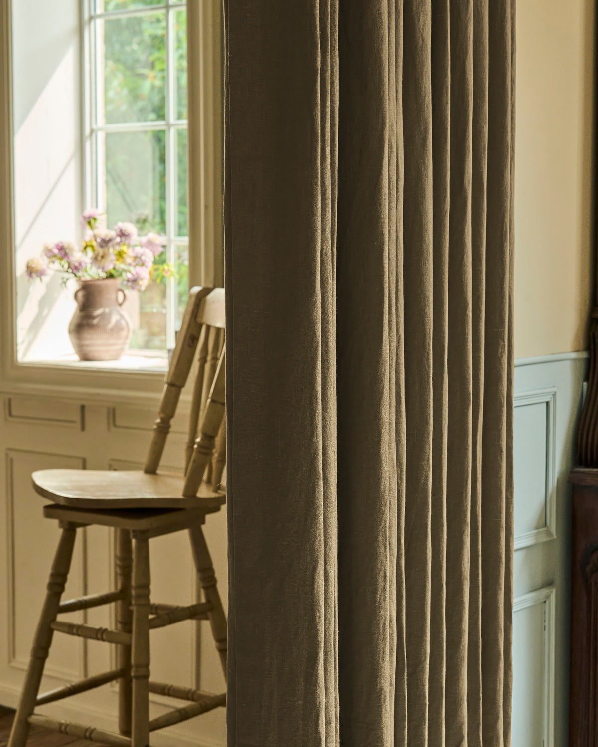 Close-up of a luxurious Helena 100% linen custom curtain panel in a warm natural shade, draped by a sunlit window.