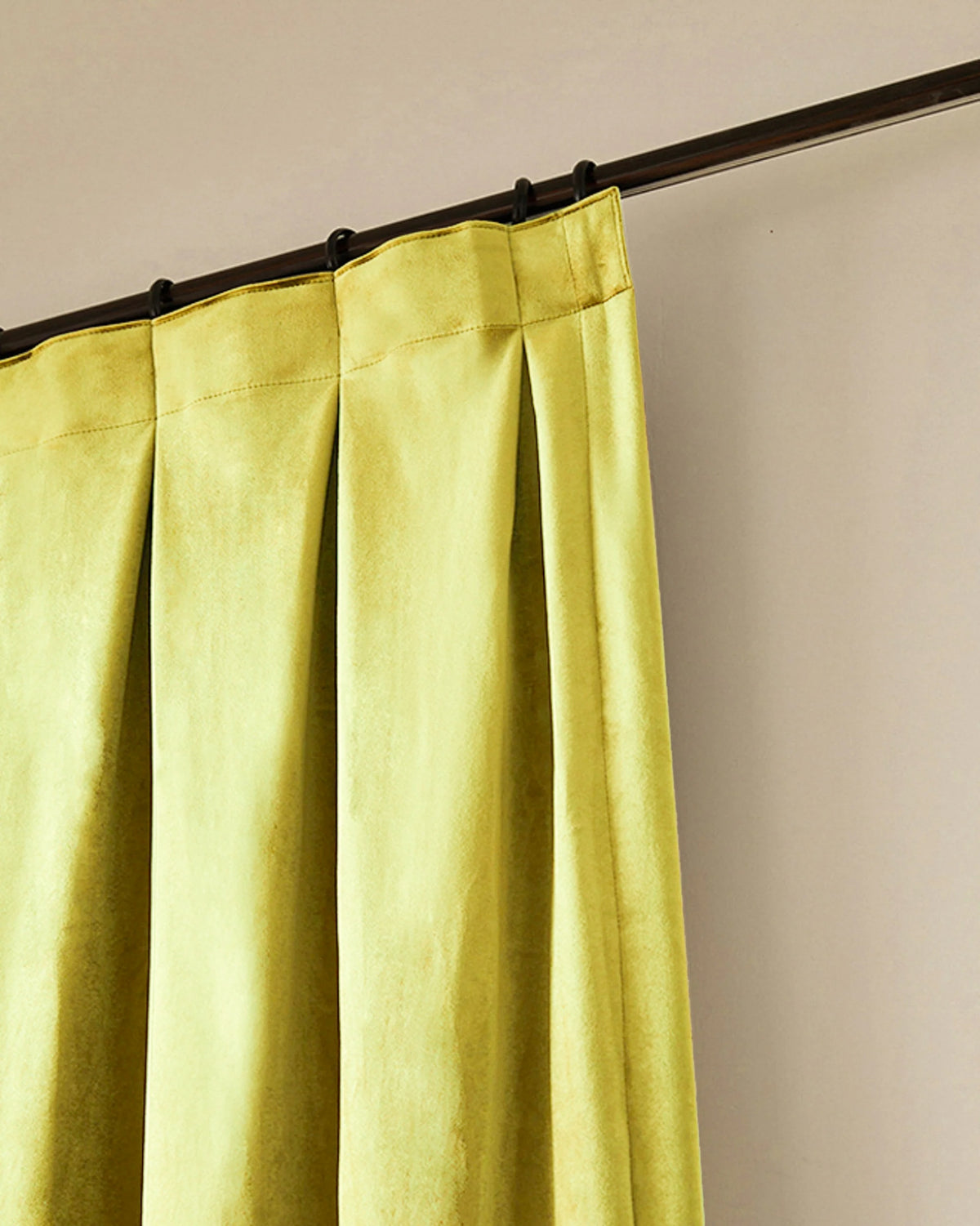 Detail of TheHues' chartreuse Moonlit Velvet custom curtain, showcasing elegant tailored pleats and rich velvet fabric on a dark rod.