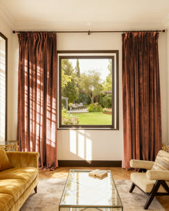 Elegant custom Moonlit rust velvet blackout curtains in a living room, offering thermal & soundproof window treatments with garden view.