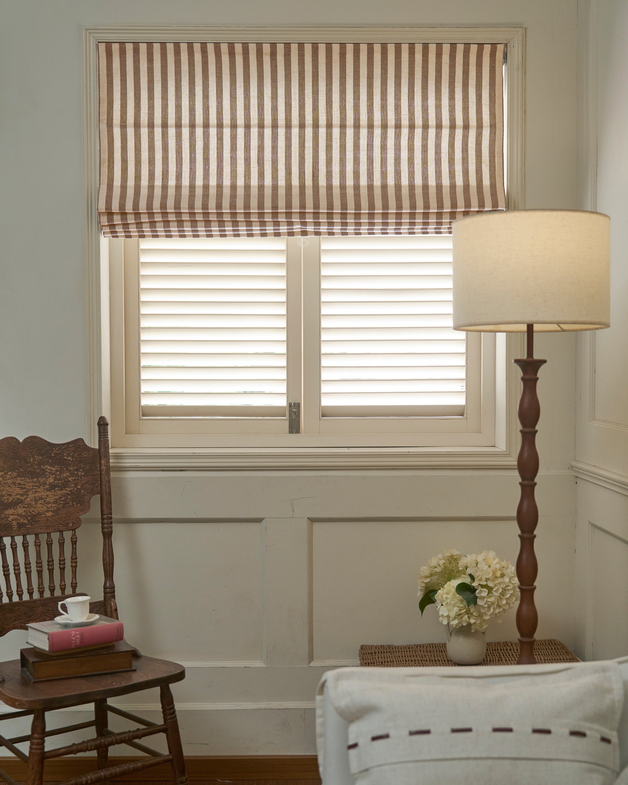 Custom-made Milano flat fold Roman shade in striped linen blend fabric, showcasing crisp folds over white window shutters.