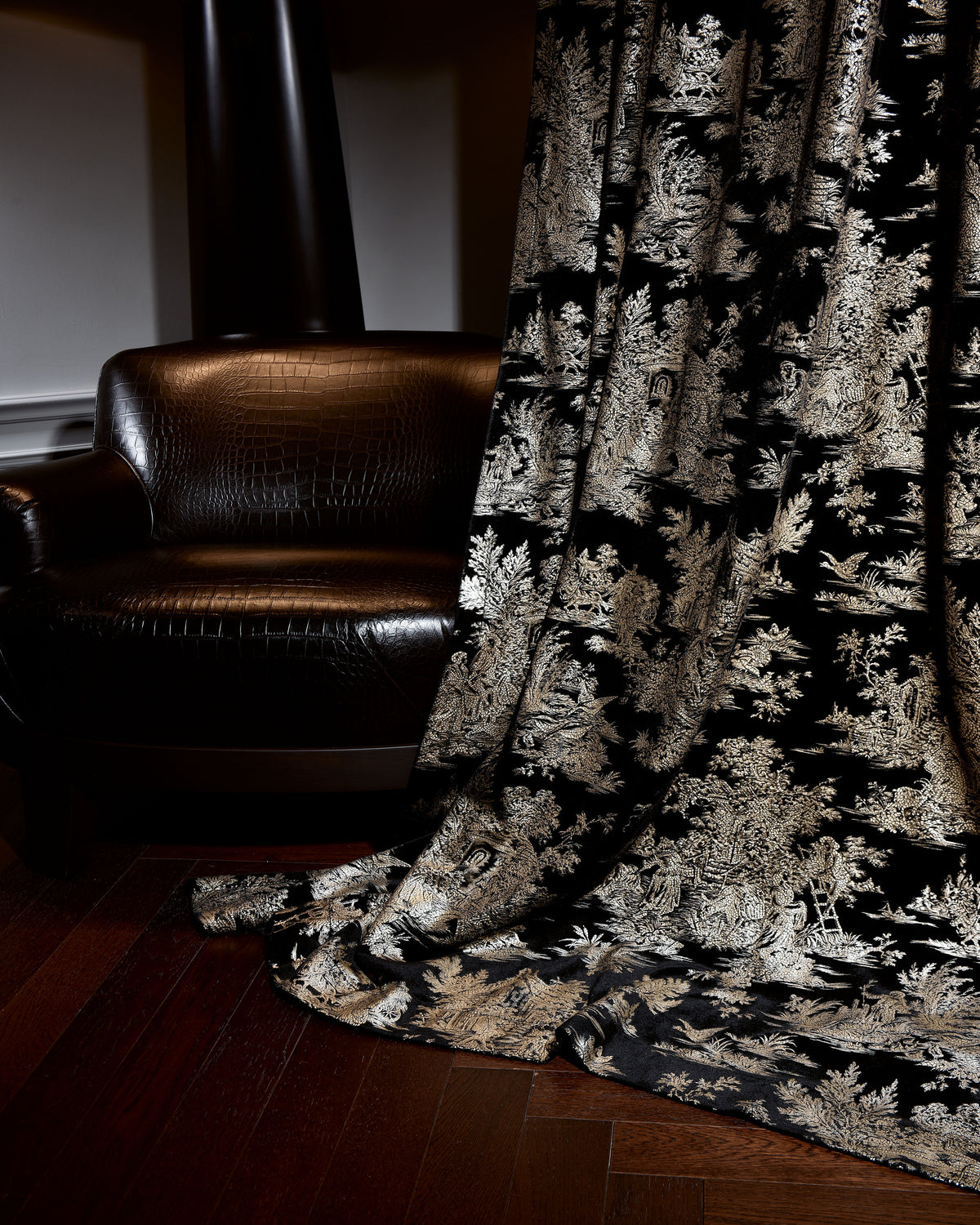 Zen foil printed black velvet custom curtain, designed in Italy, showcasing intricate gold patterns, draped beside a dark leather armchair.