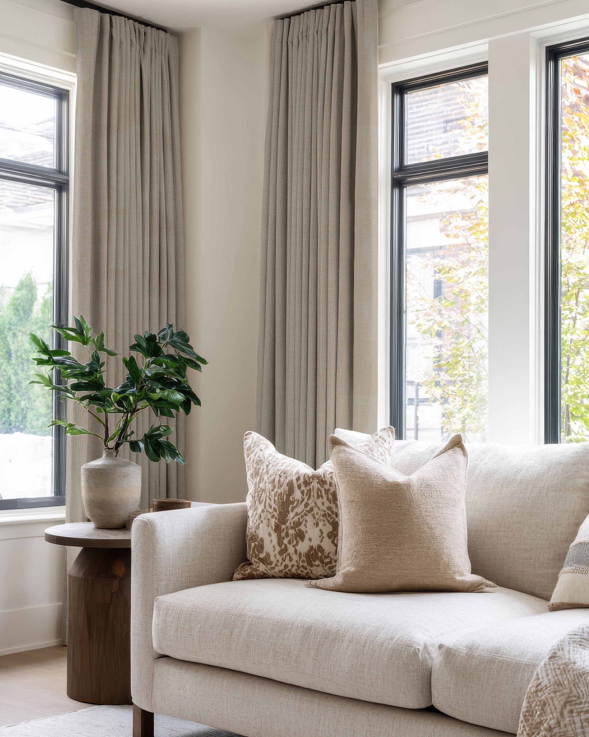 Zoe linen look custom blackout curtains frame large windows, enhancing a neutral living room's sophisticated aesthetic.