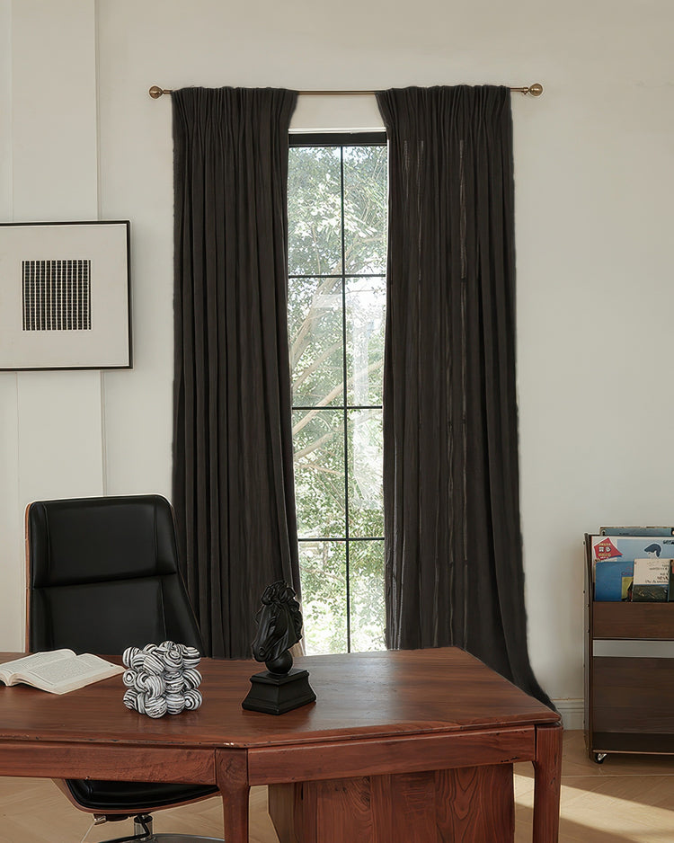 Pair of custom Ivy linen look heavyweight herringbone textured curtains in dark gray, hanging on a brass rod in a bright room.