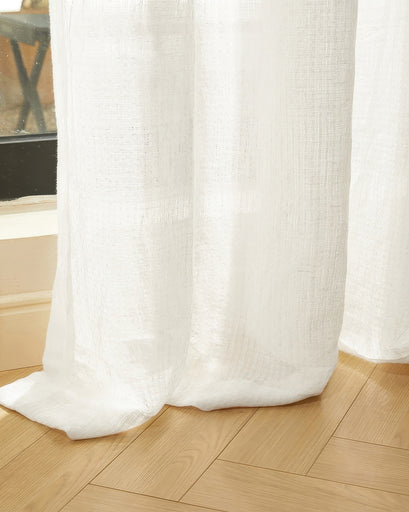 White Unwind Linen Blend sheer custom curtain with a subtle grid-like weave, pooling elegantly on a light wood floor.