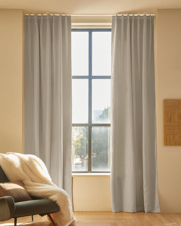 Soft grey Latvian linen blend custom curtains with elegant pleat header framing a tall window, offering light control & sophisticated home aesthetics.