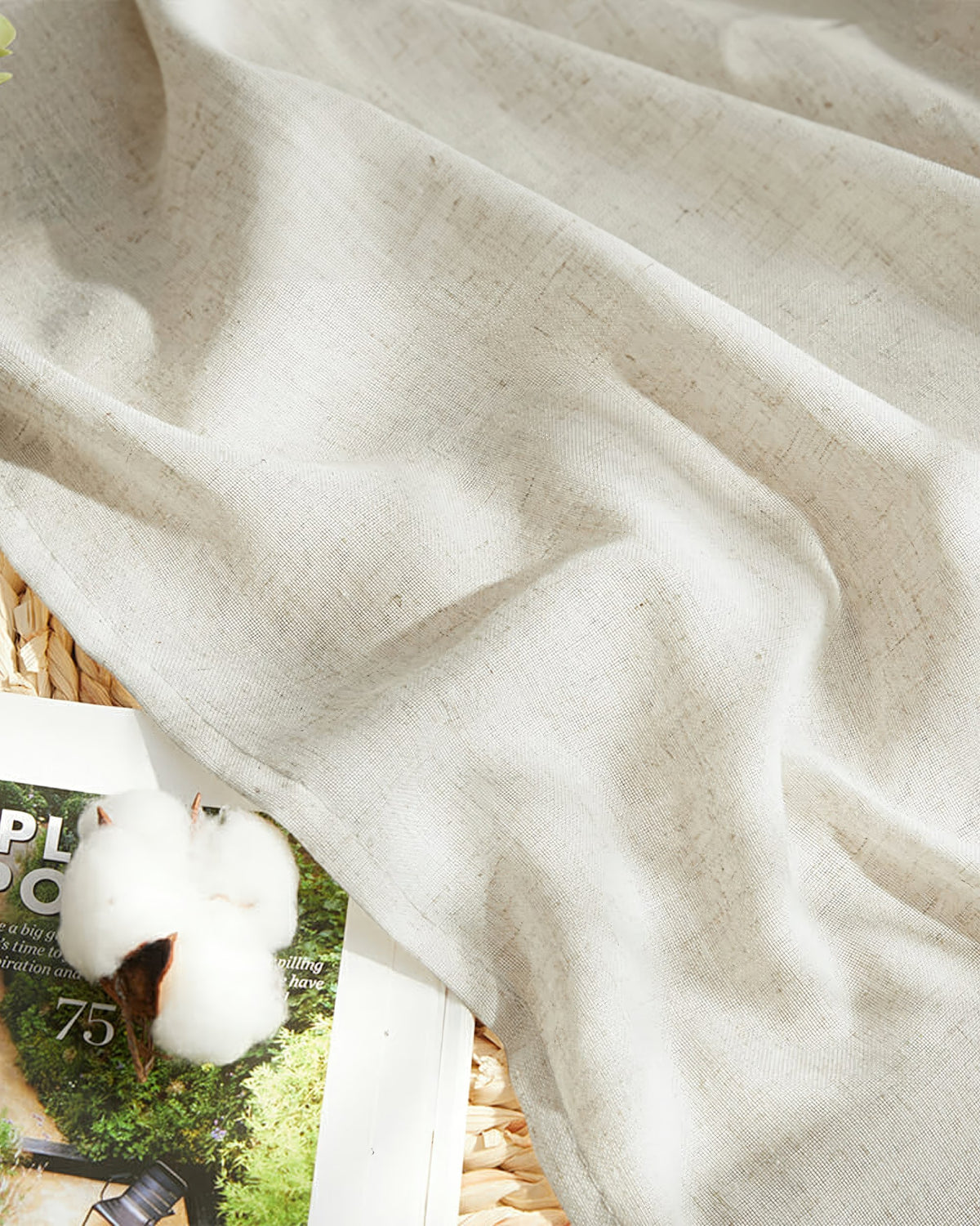 Detail of Noah linen-look lightweight outdoor curtain fabric, draped, with a cotton boll and magazine, emphasizing its natural beige texture.