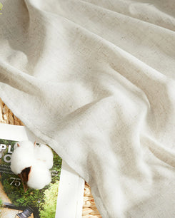 Detail of Noah linen-look lightweight outdoor curtain fabric, draped, with a cotton boll and magazine, emphasizing its natural beige texture.