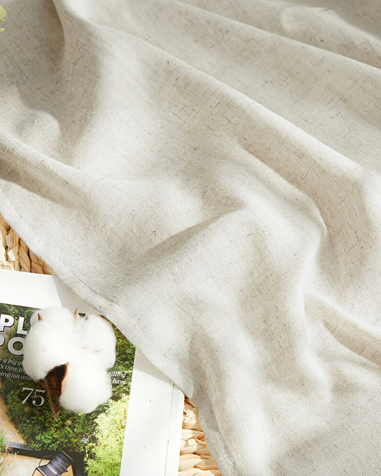 Detail of Noah linen-look lightweight outdoor curtain fabric, draped, with a cotton boll and magazine, emphasizing its natural beige texture.