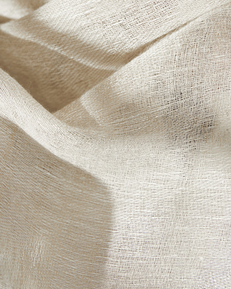 Close-up of a light beige, loosely woven linen blend sheer curtain fabric, showcasing its delicate texture and soft drapery.