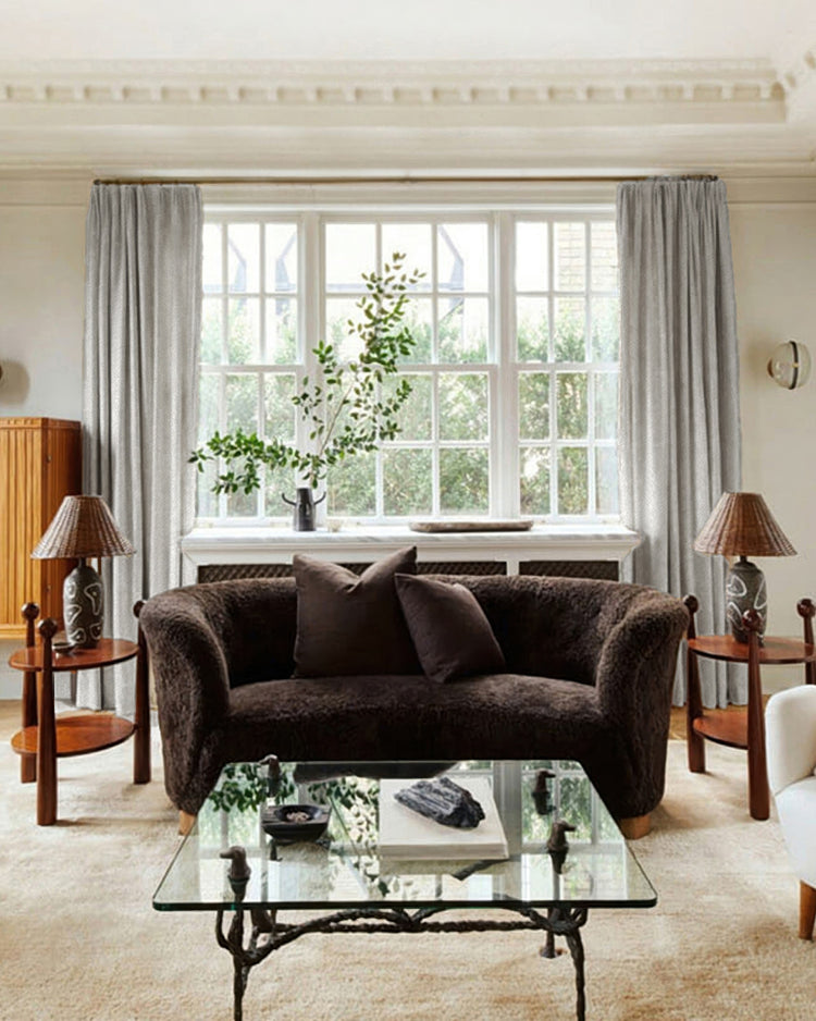 Elegant light grey Voy Linen Look custom curtains frame a large window in a luxury living room, featuring a dark brown sofa & glass table.