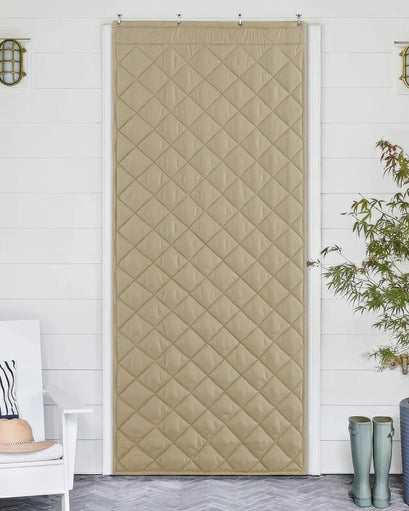 Beige quilted custom door curtain, offering thermal insulation & soundproofing, hanging on a white door in a stylish home setting.
