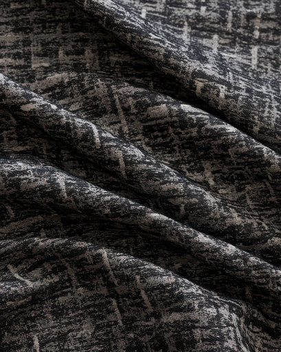 Close-up of draped Glint custom curtain fabric, featuring a shimmering linen blend textured with an abstract black & grey pattern.
