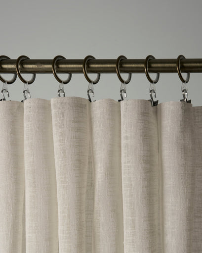 Cream Sunveil pure linen sheer custom curtain close-up, highlighting textured fabric, elegant folds & ring clip header on bronze rod.