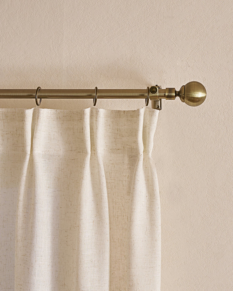Antique brass ball finial custom curtain rod with cream pinch pleat linen drapery panel for elegant window treatments.