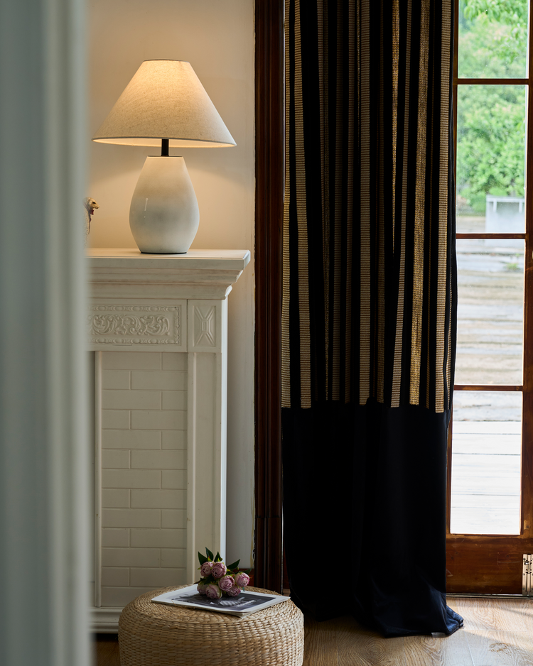Renee custom striped linen velvet color block drapery featuring black & gold stripes, solid black panel, by a window & fireplace.