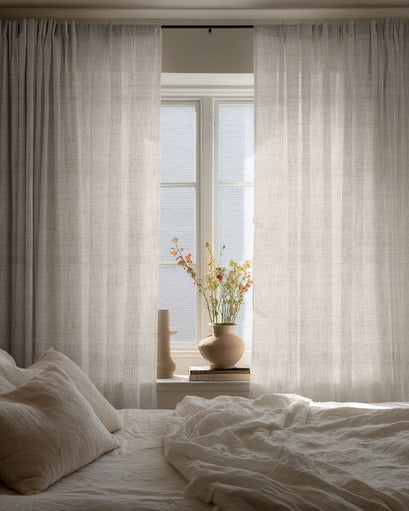 Custom Sunveil linen sheer curtains softly filter light in a tranquil bedroom with white linen bedding.