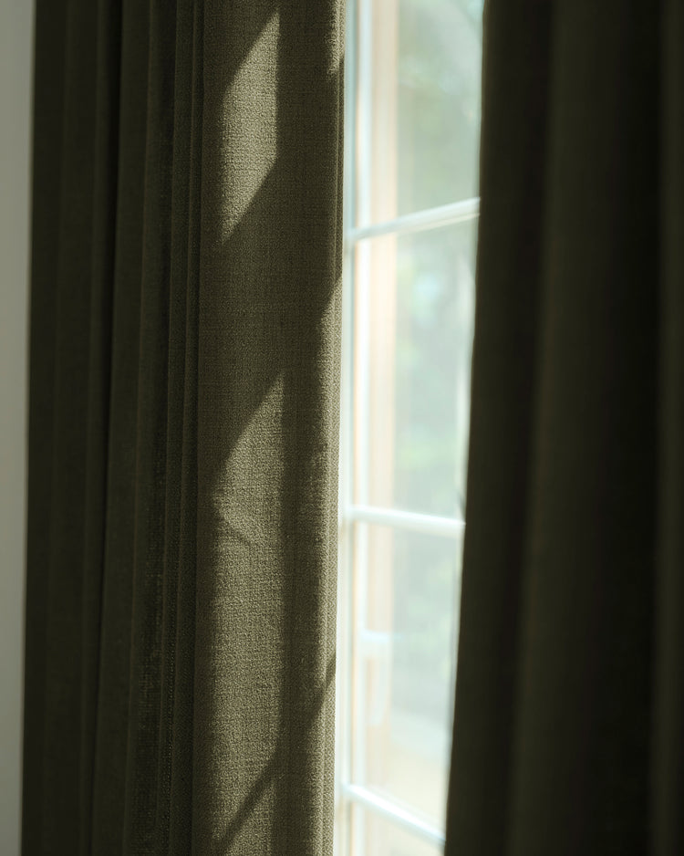 Close-up of elegant Iris textured custom drapery in rich olive, highlighting fabric texture & tailored look against a sunlit window.