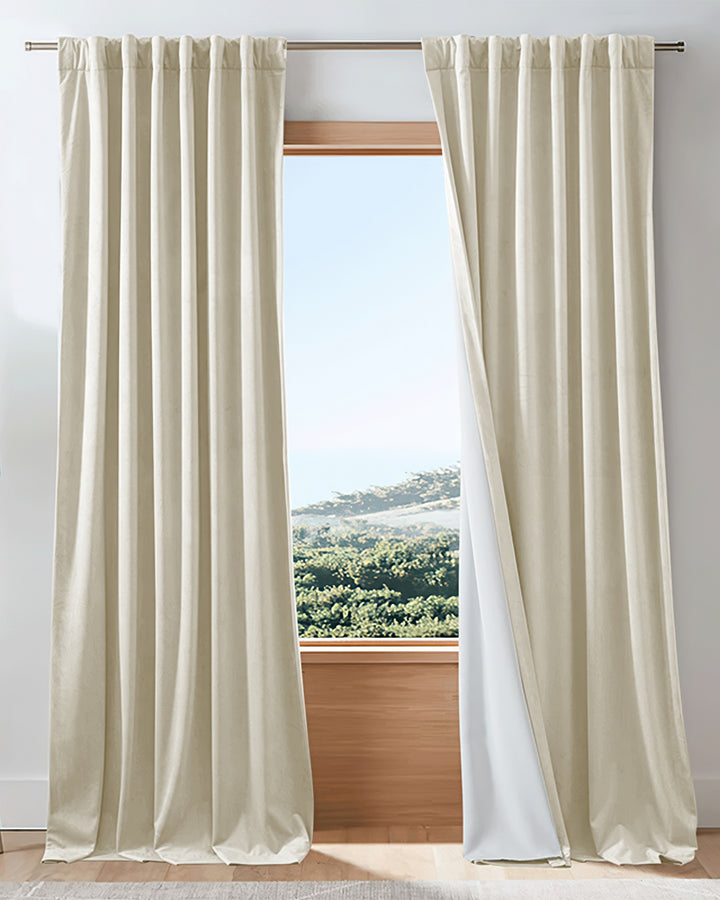 Creamy velvet custom blackout drapery, showing its thermal soundproof lining, elegantly framing a bright window view.