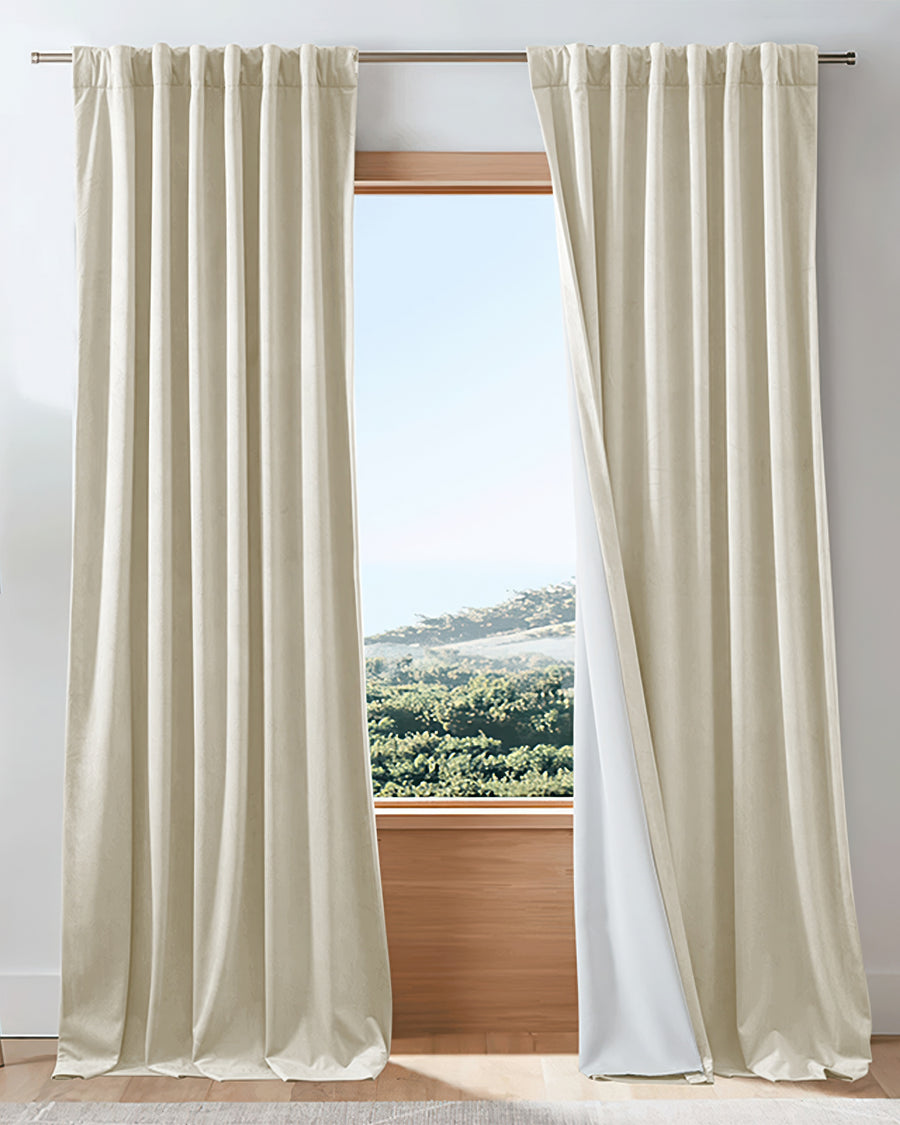 Creamy velvet custom blackout drapery, showing its thermal soundproof lining, elegantly framing a bright window view.