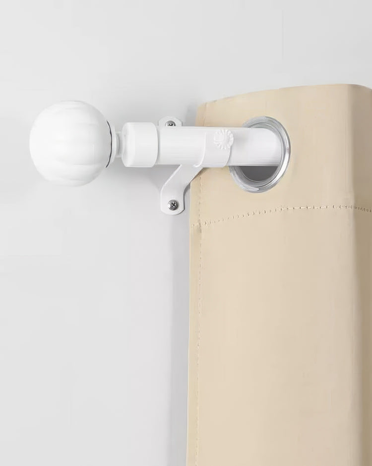 White reeded ball finial on an adjustable curtain rod with a beige grommet curtain, showcasing elegant window treatment hardware.