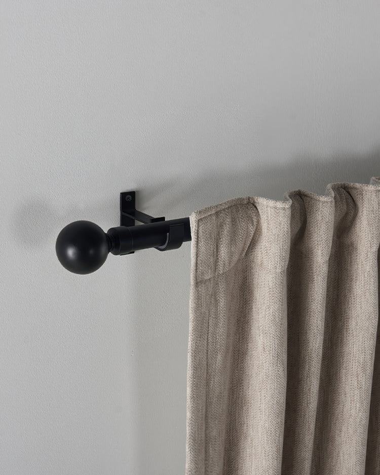 Black custom curtain rod with a sleek Roman round finial, holding a tailored beige woven drapery panel.
