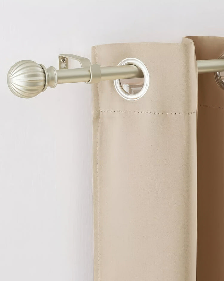 Stylish brass adjustable curtain rod with fluted finial supporting light beige grommet curtains for sophisticated window treatment.