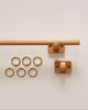 Minimal beech wood curtain rod with two matching wall mounts and six brass curtain rings for window treatments.