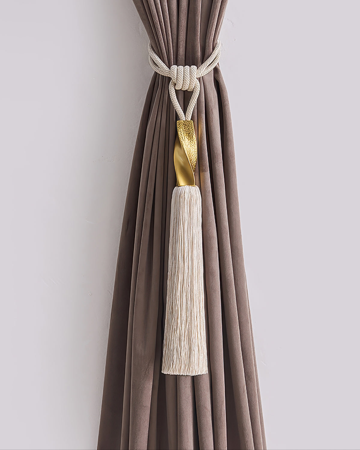 Luxurious cream rope tassel curtain tieback featuring a textured gold accent, stylishly securing a tailored brown velvet drape.