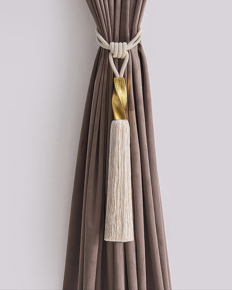 Luxurious cream rope tassel curtain tieback featuring a textured gold accent, stylishly securing a tailored brown velvet drape.