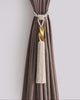 Luxurious cream rope tassel curtain tieback featuring a textured gold accent, stylishly securing a tailored brown velvet drape.