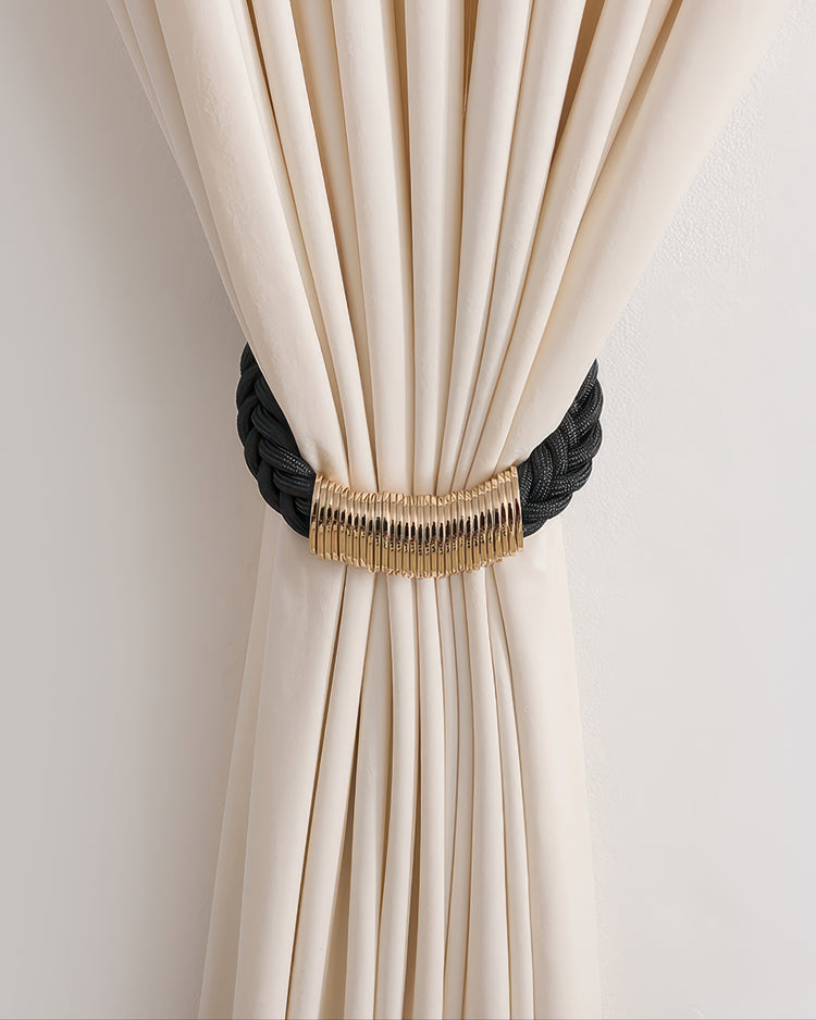 Black braided rope curtain tieback with elegant gold rings, neatly securing a cream drapery panel for a refined window treatment.