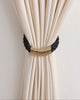 Black braided rope curtain tieback with elegant gold rings, neatly securing a cream drapery panel for a refined window treatment.