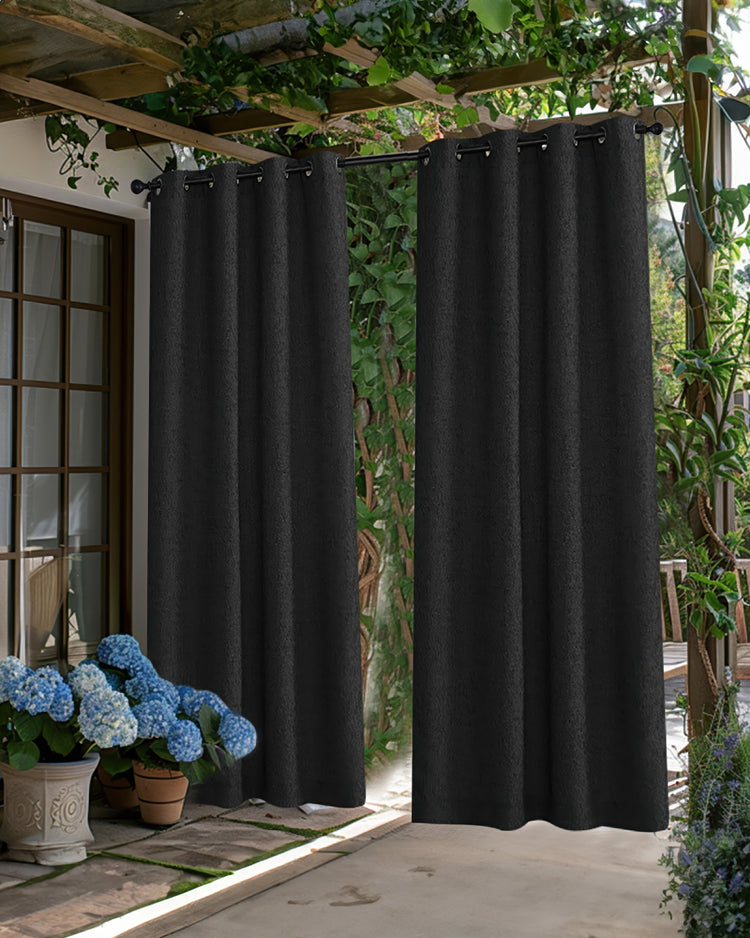 Two black Munich woven textured waterproof custom outdoor curtains with grommet tops, hanging under a patio pergola.