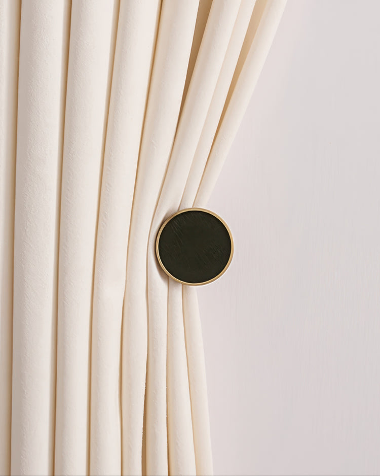 Cream velvet custom drapery gathered by a dark fur textured circular curtain wall hook with elegant gold trim.