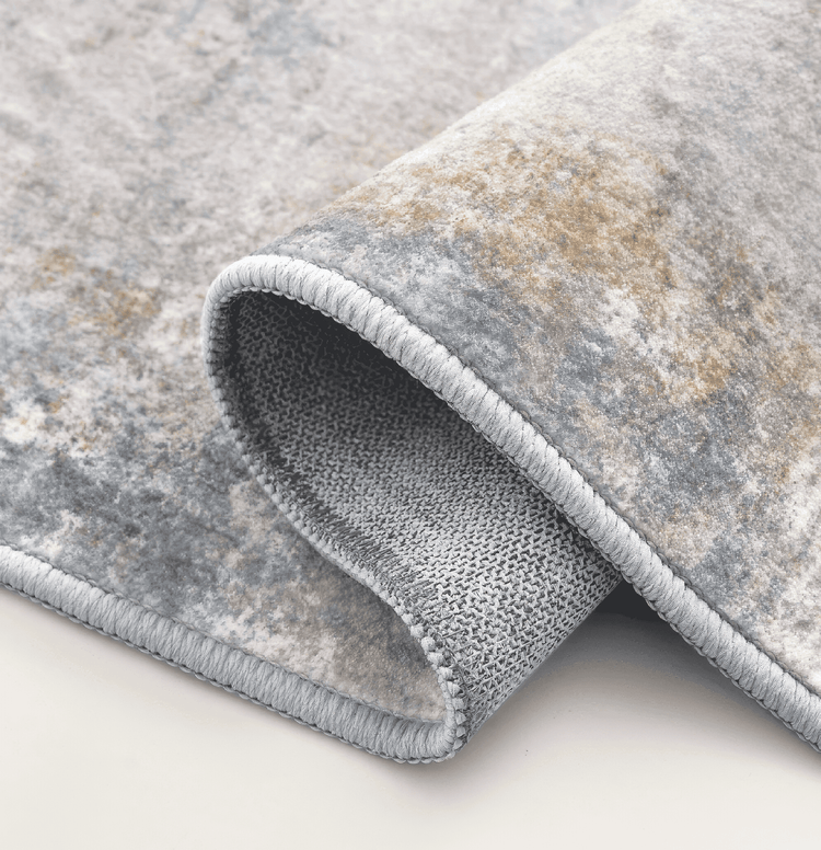 Mystic Clouds washable area rug, partially rolled to show abstract grey/blue pattern, serged edge, & textured non-slip backing.